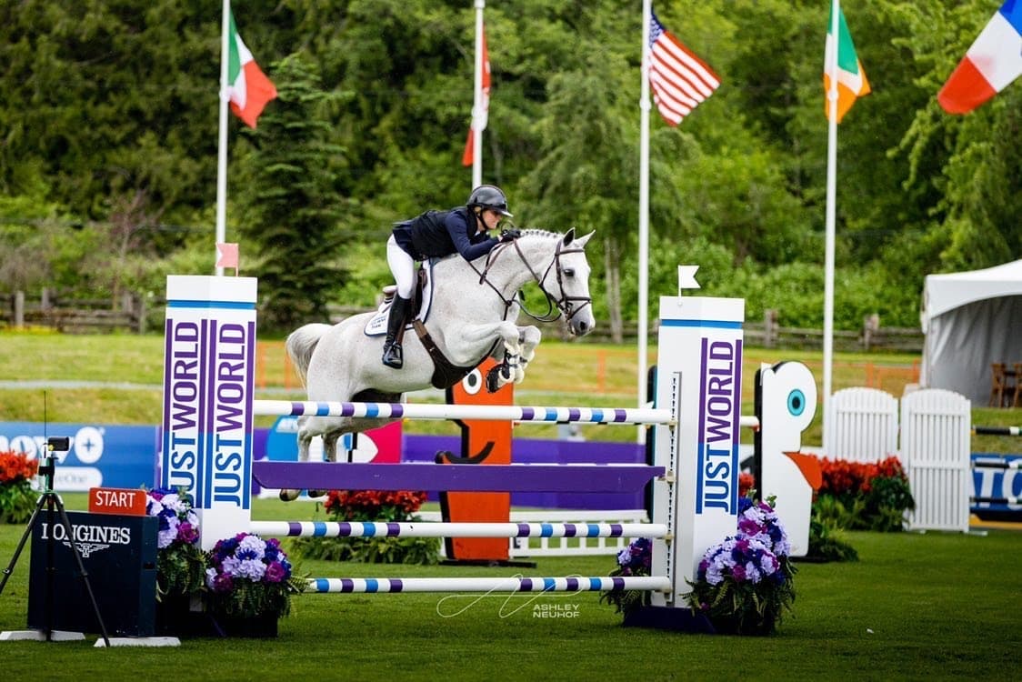 Emma Marlowe and a grey horse over an oxer on the grass grand prix field in Vancouver